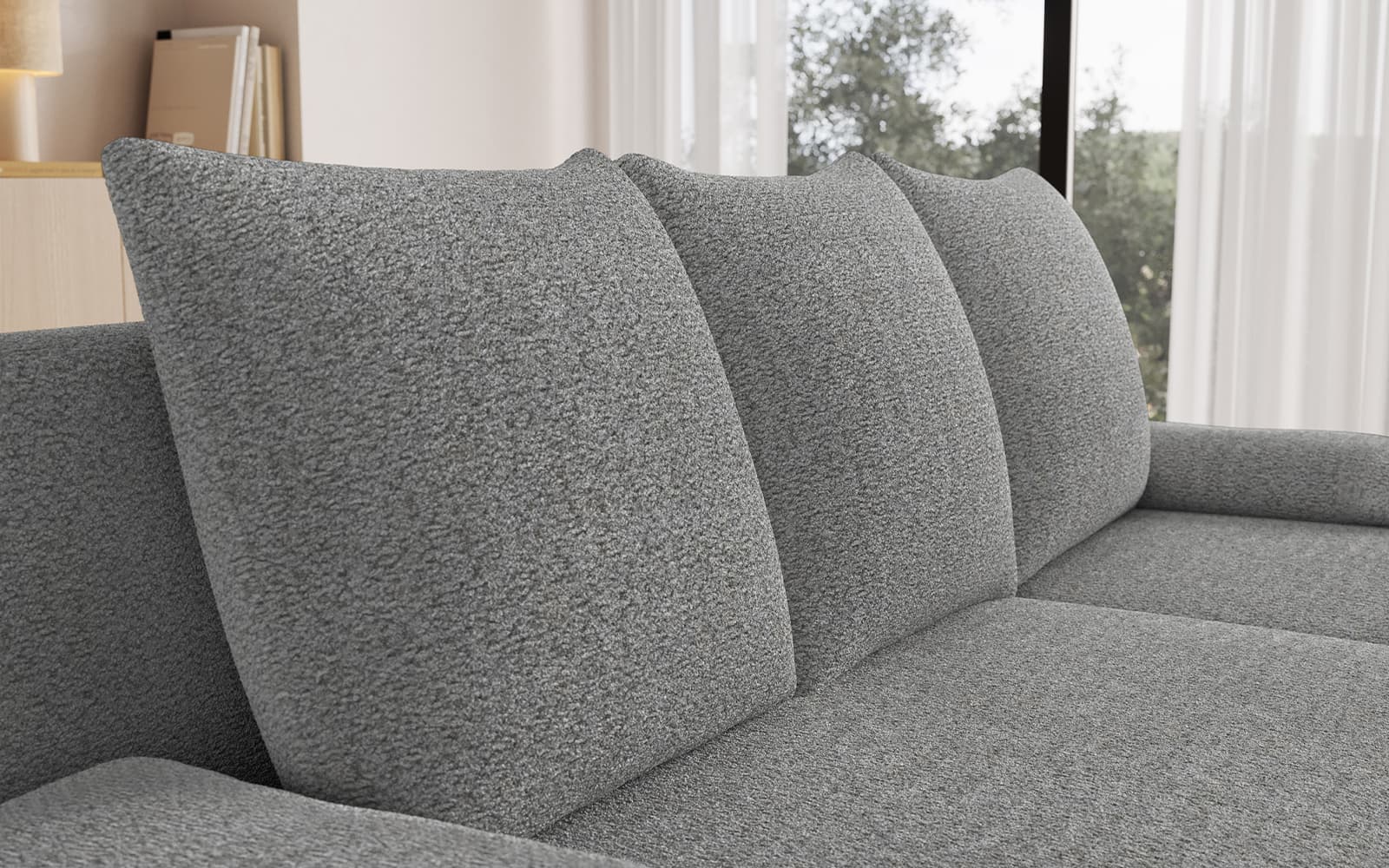 Close-up of a light gray upholstered sofa with three back cushions in a bright living room.